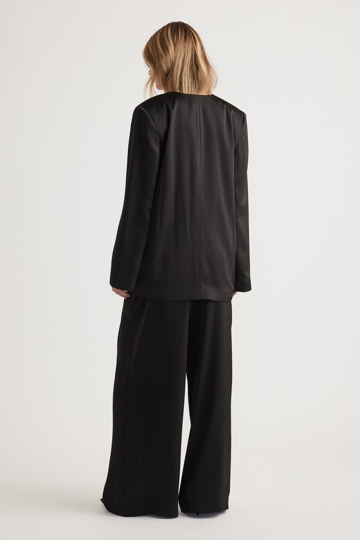 Woman wearing black wide-leg pants and a matching long sleeve blazer with relaxed fit, viewed from behind.