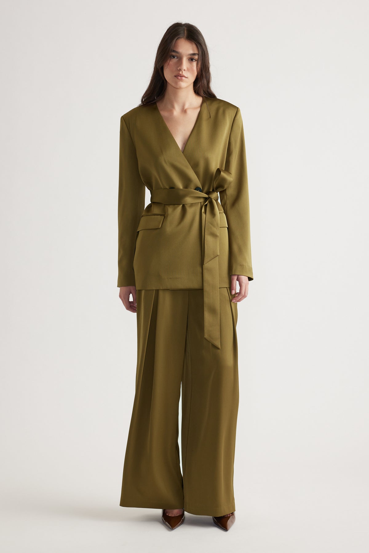 Woman wearing an olive green wrap blazer with belt paired with matching wide-leg pants and brown pointed heels
