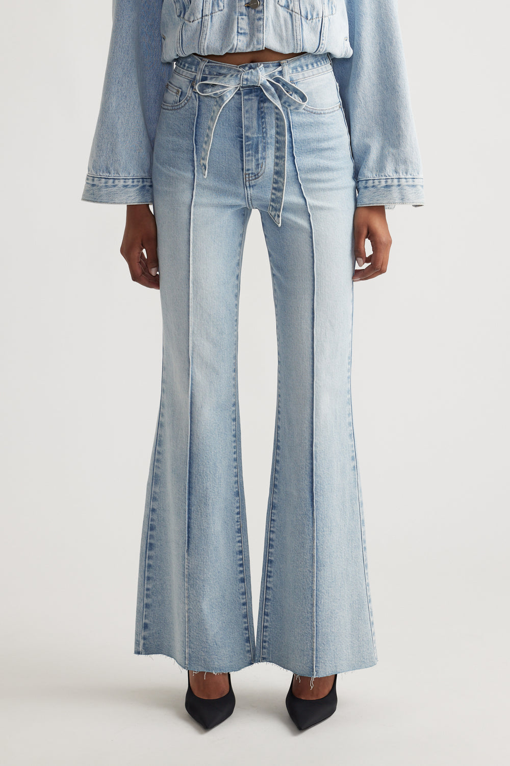 Woman wearing light blue Freya Flare Jean with a tied waist belt, styled with matching denim jacket and black heels