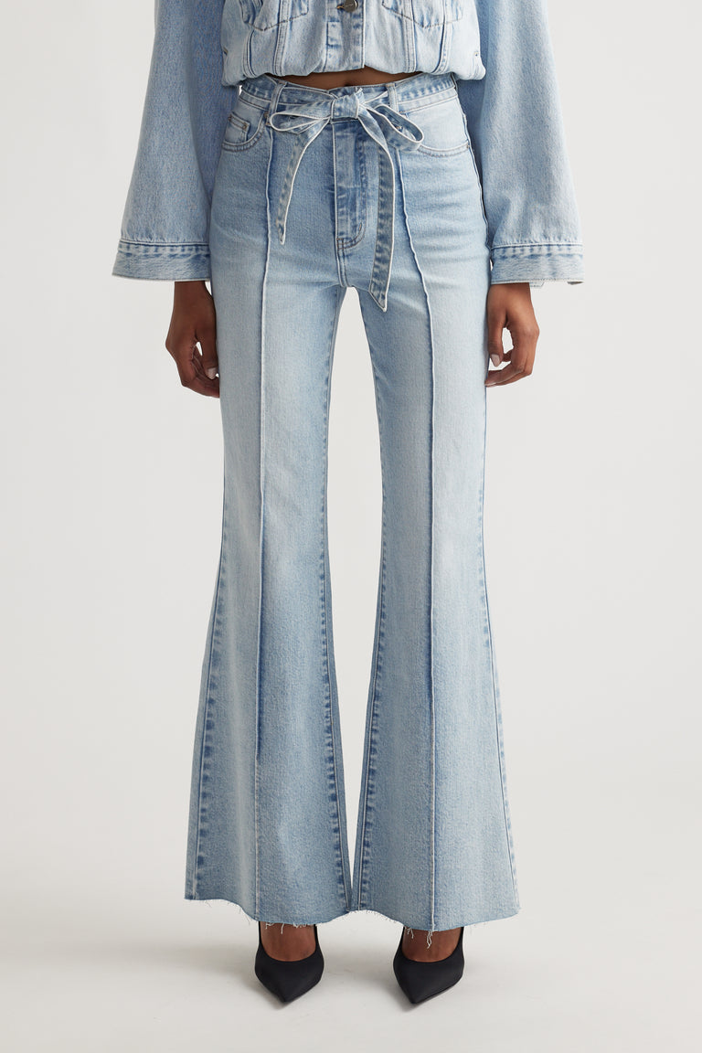 Woman wearing light blue Freya Flare Jean with a tied waist belt, styled with matching denim jacket and black heels
