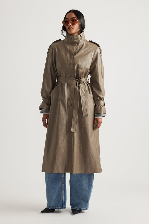 Woman wearing a taupe faux leather trench coat with a belted waist, styled with wide-leg denim jeans and sunglasses