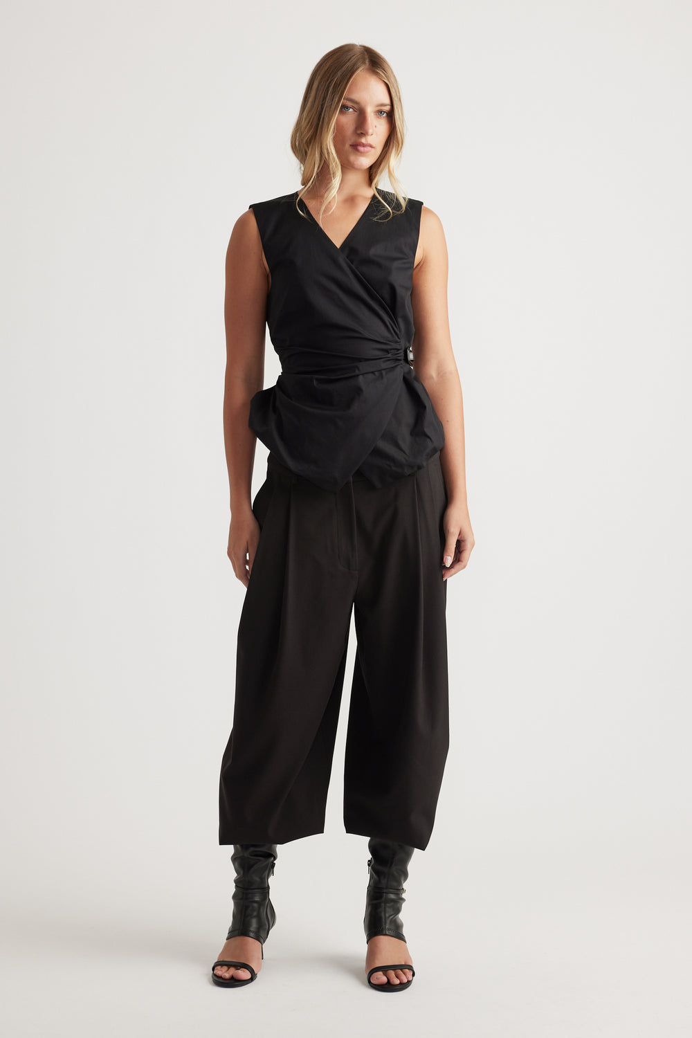 Woman wearing Ava Belted Wrap Top in black with sleeveless cut and adjustable side belt, styled with wide-leg pants by DECJUBA