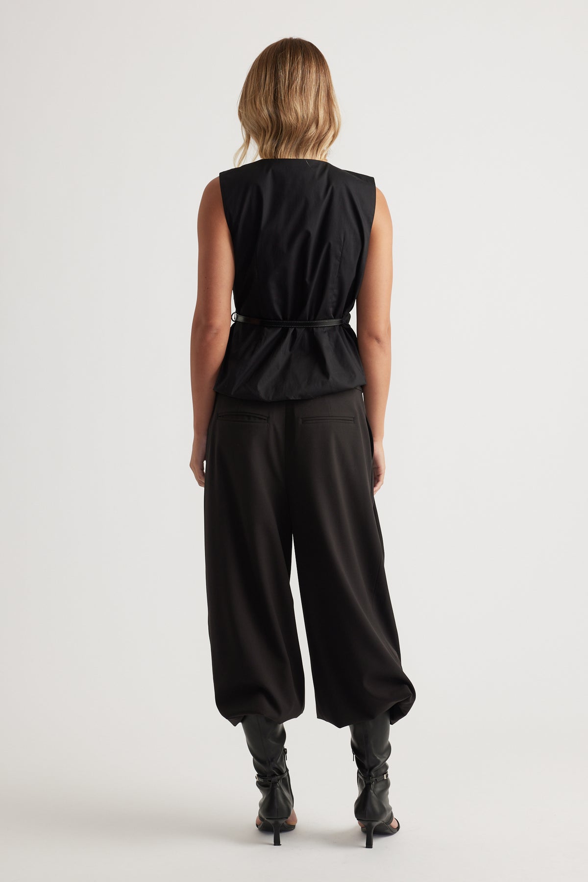 Woman seen from behind wearing Ava Belted Wrap Top in black with sleeveless design and slim belt by DECJUBA