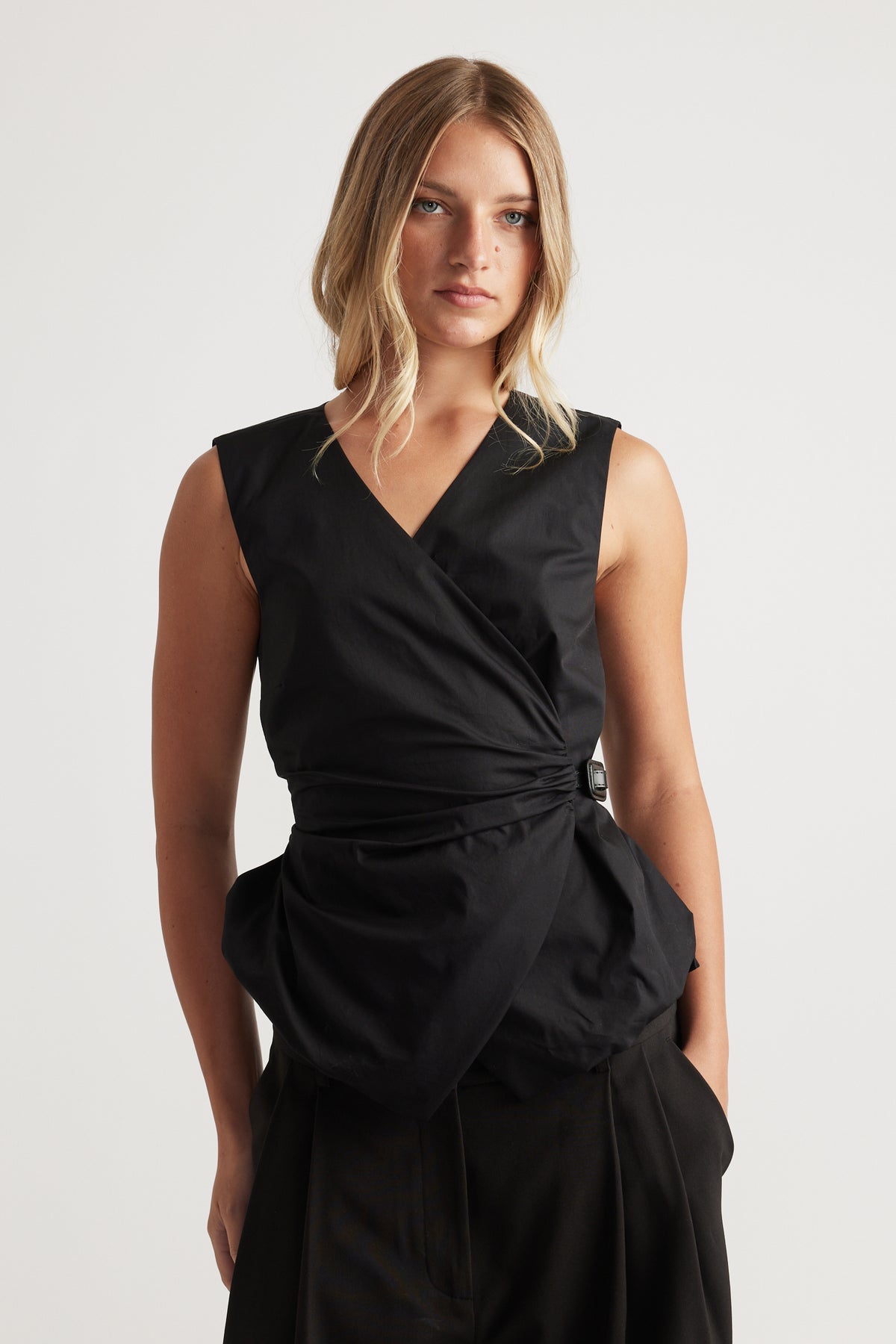 Woman wearing Ava Belted Wrap Top in black with sleeveless fit and side tie detail by DECJUBA, an effortless versatile style.