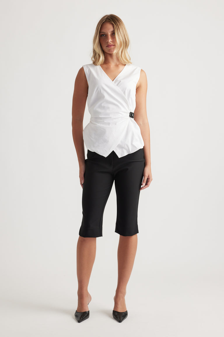 Woman wearing a sleeveless white wrap top with a side buckle paired with fitted black cropped pants and black heels