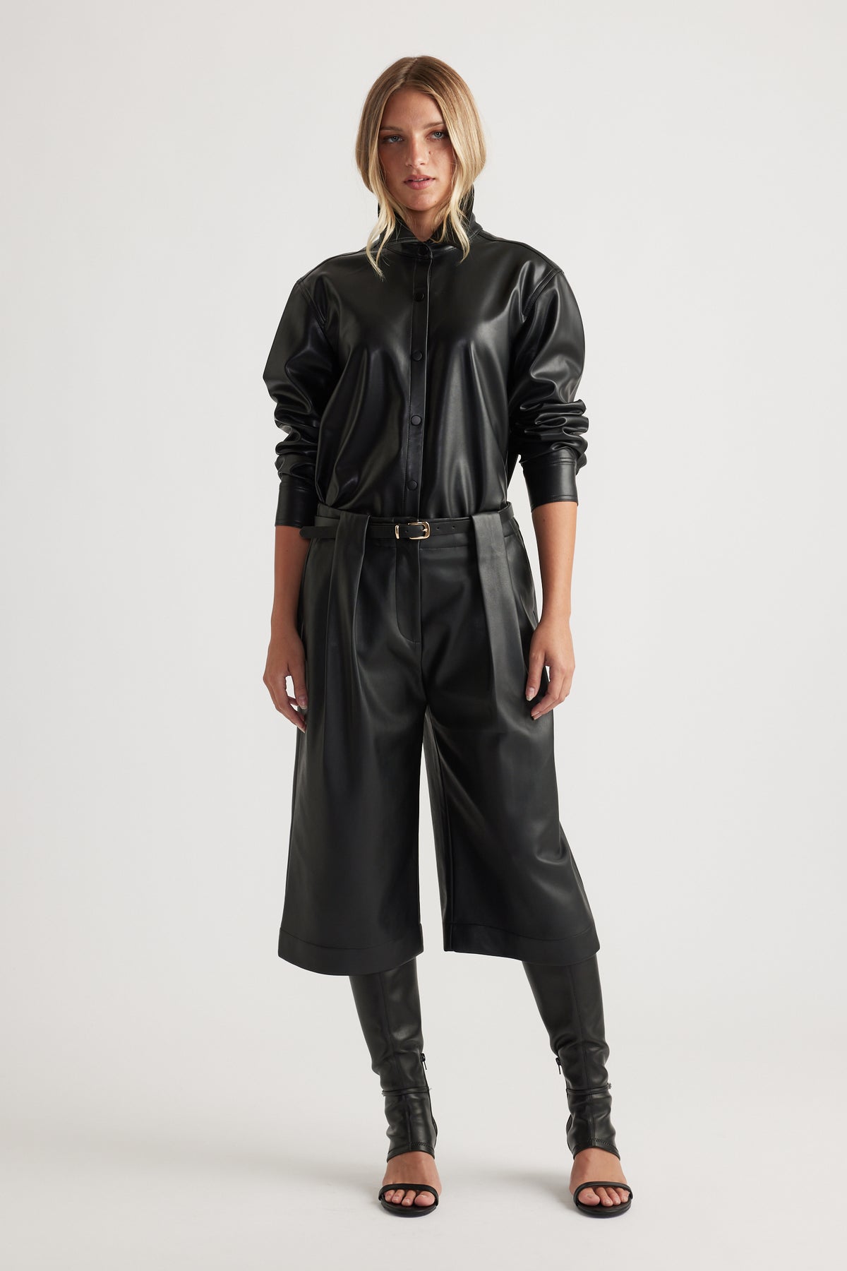 Woman wearing Tabitha Faux Leather Short in black with high waist and wide leg, paired with matching leather shirt by DECJUBA