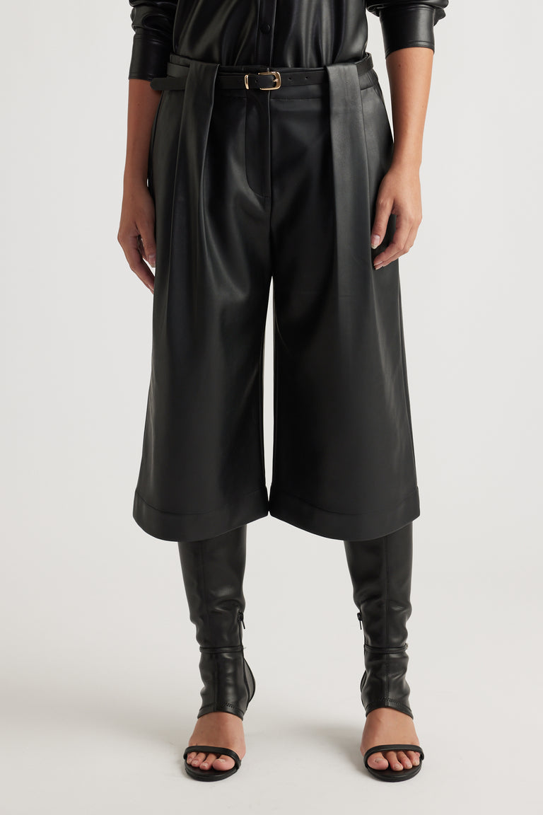 Woman wearing Tabitha Faux Leather Short in black with pleated front and belted waist, styled with matching boots by DECJUBA