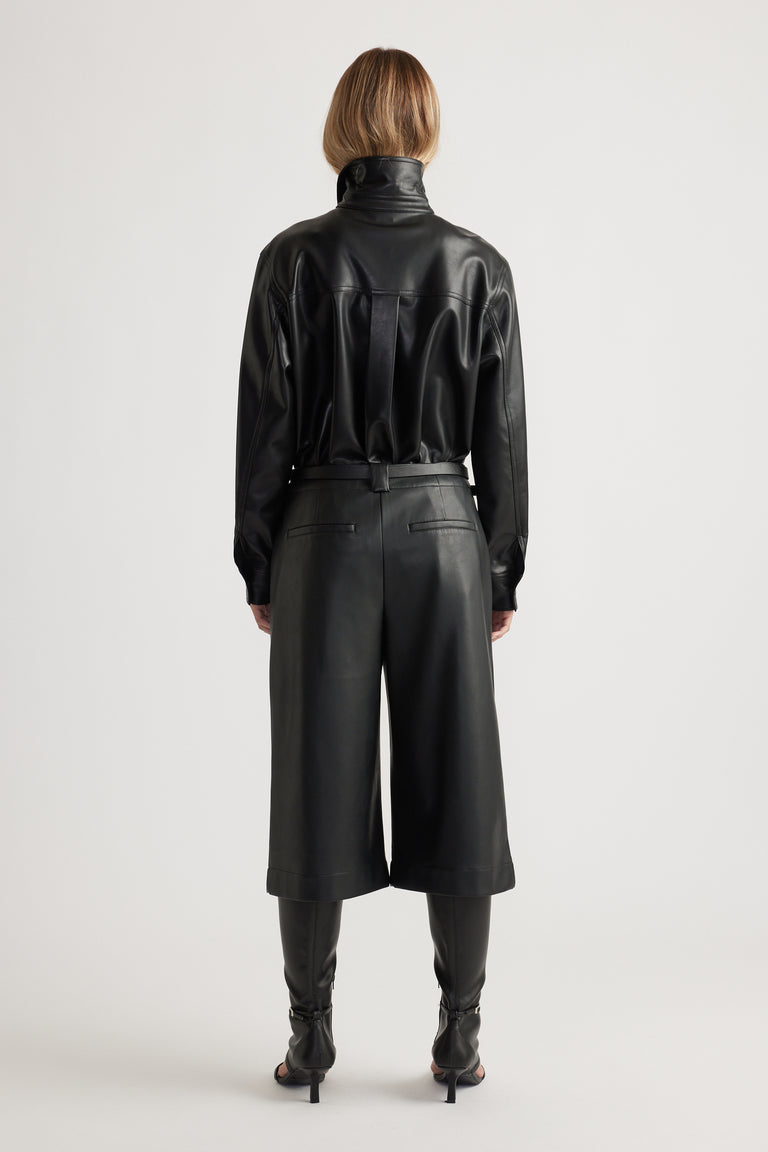 Woman shown from behind wearing Tabitha Faux Leather Short in black, styled with coordinating long-sleeve leather top and boots by DECJUBA