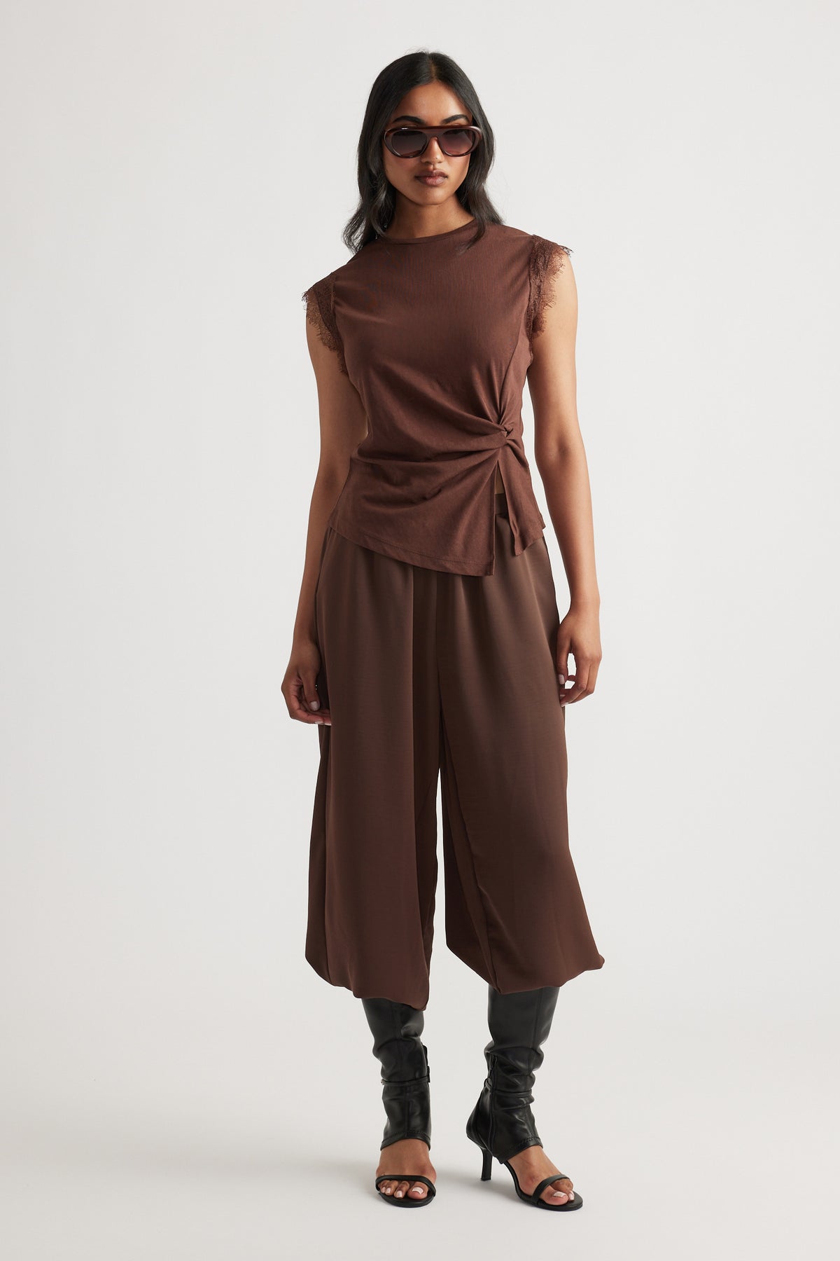 Woman wearing a sleeveless teak brown top with side tie detail paired with wide-leg cropped pants and black heeled boots