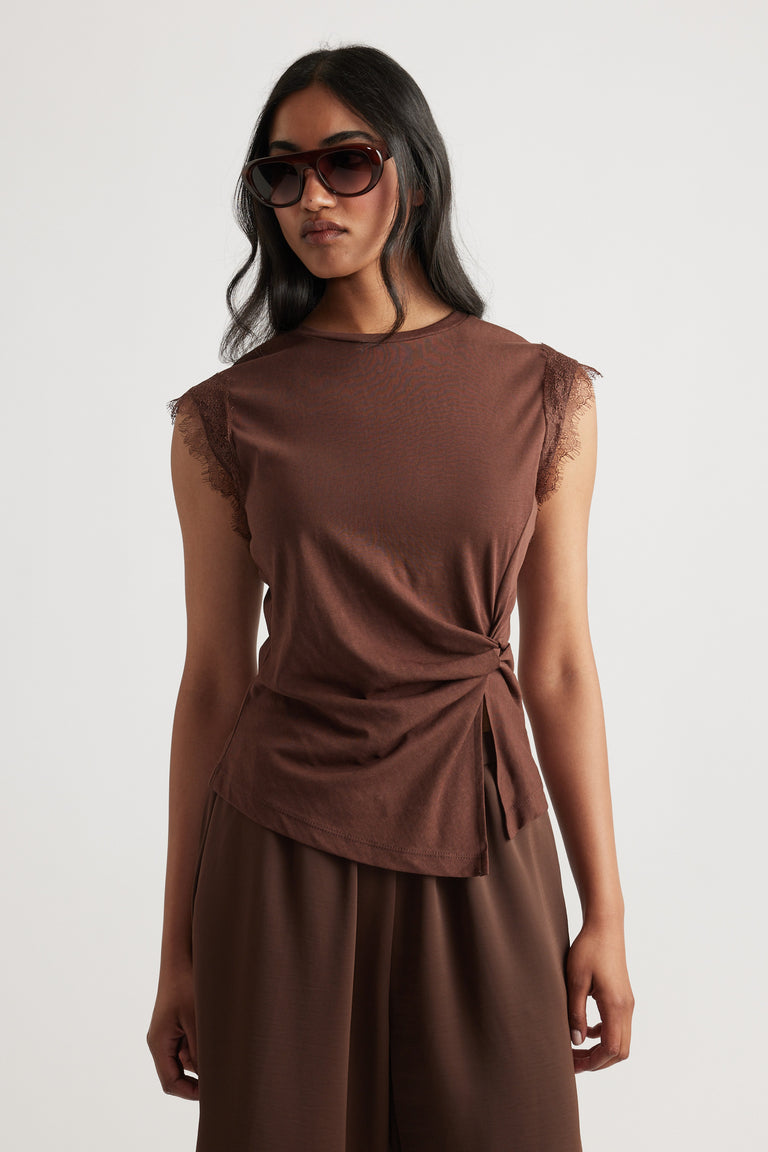 Woman wearing a sleeveless brown top with lace trim at the shoulders and a side tie detail paired with matching pants