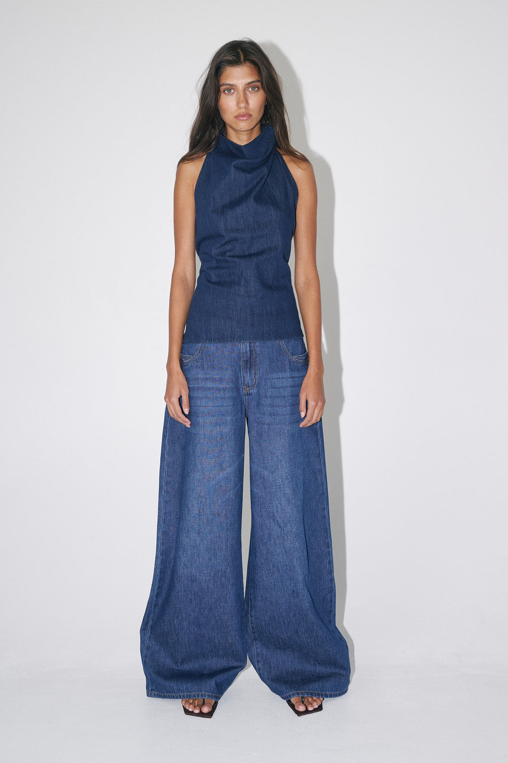 Woman wearing super wide-leg blue jeans with a sleeveless navy top and sandals