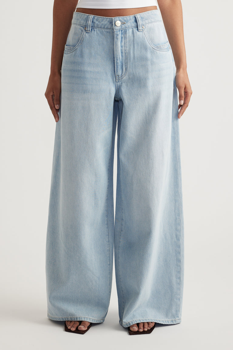 Model wearing light blue mid rise jeans with a relaxed fit and super wide legs