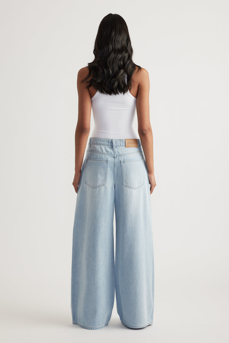 Model viewed from behind wearing light blue mid rise super wide leg jeans and a white tank top