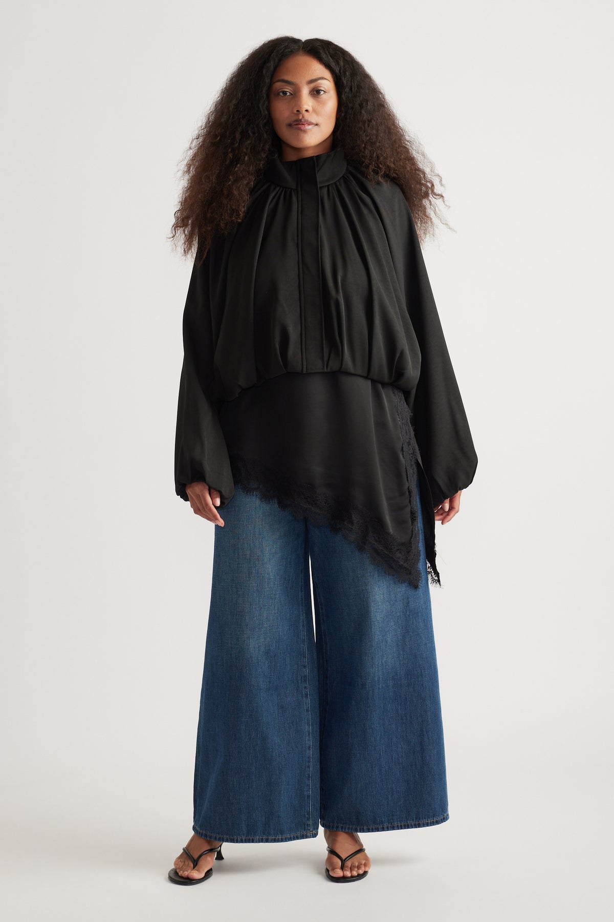 Woman wearing a black gathered blouse with full-length wide-leg blue jeans and flat sandals