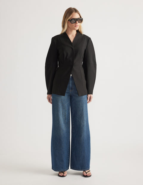 Woman wearing a tailored black blazer paired with wide leg denim jeans and black open-toe heels and sunglasses