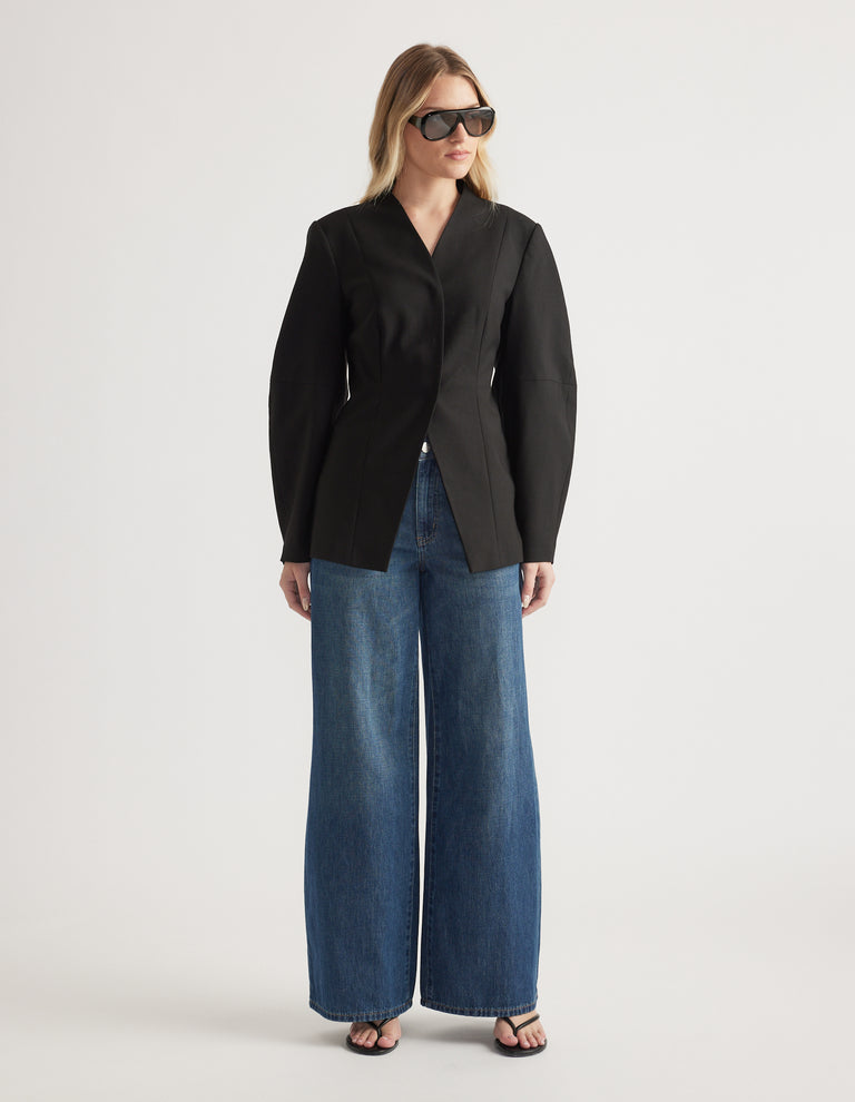 Woman wearing a tailored black blazer paired with wide leg denim jeans and black open-toe heels and sunglasses