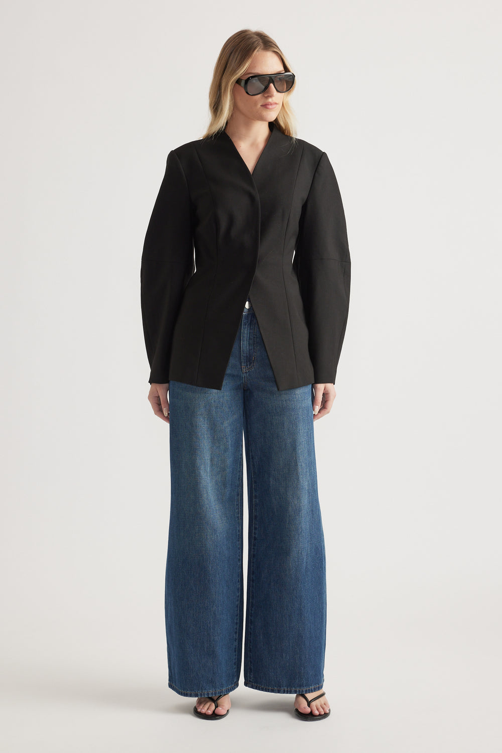Woman wearing a black tailored blazer with barrel sleeves, wide-leg blue jeans and sunglasses