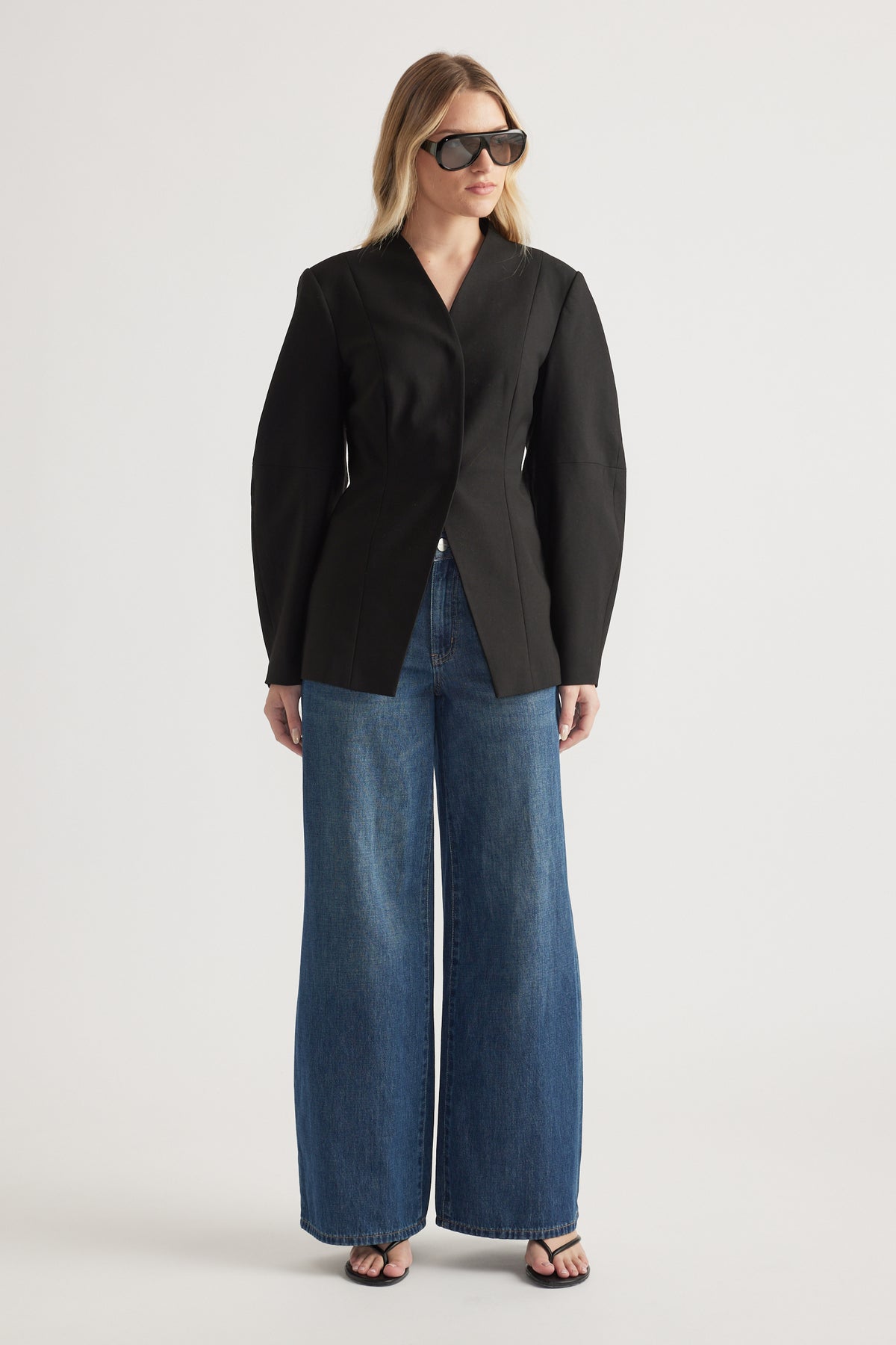 Woman wearing a black tailored blazer with barrel sleeves, wide-leg blue jeans and sunglasses