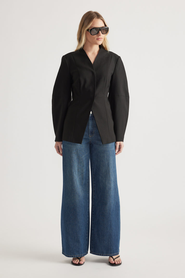 Woman wearing a black tailored blazer with barrel sleeves, wide-leg blue jeans and sunglasses