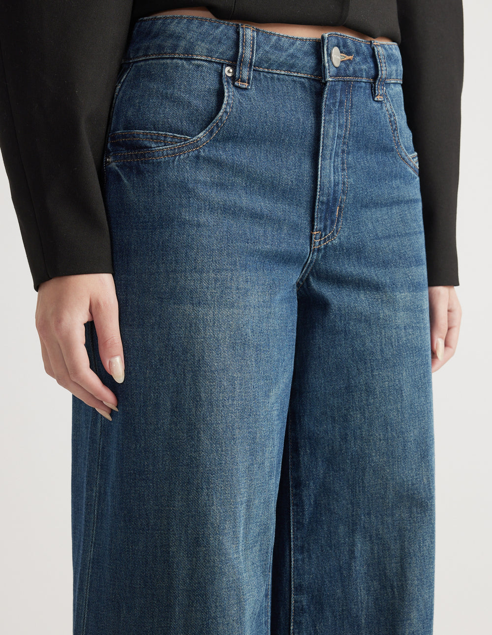 Close-up of mid-rise wide-leg jeans in classic blue denim with front pockets and belt loops paired with a black top
