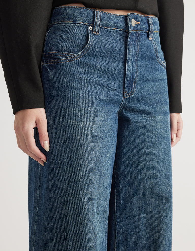 Close-up of mid-rise wide-leg jeans in classic blue denim with front pockets and belt loops paired with a black top