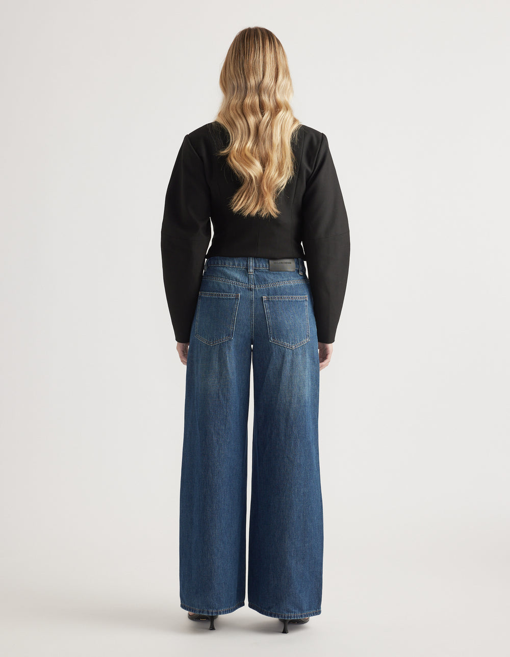 Woman wearing mid-rise wide-leg denim jeans paired with a fitted black long-sleeve top and heels