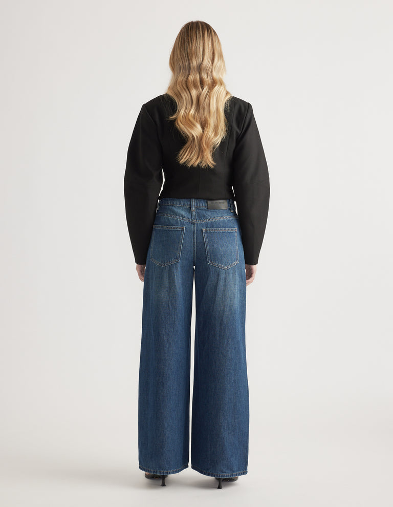 Woman wearing mid-rise wide-leg denim jeans paired with a fitted black long-sleeve top and heels