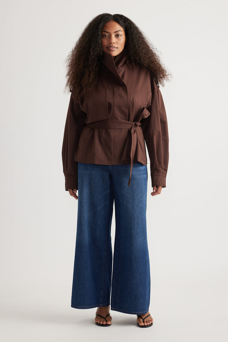 Woman wearing a belted brown jacket with full-length wide-leg blue jeans and flat sandals