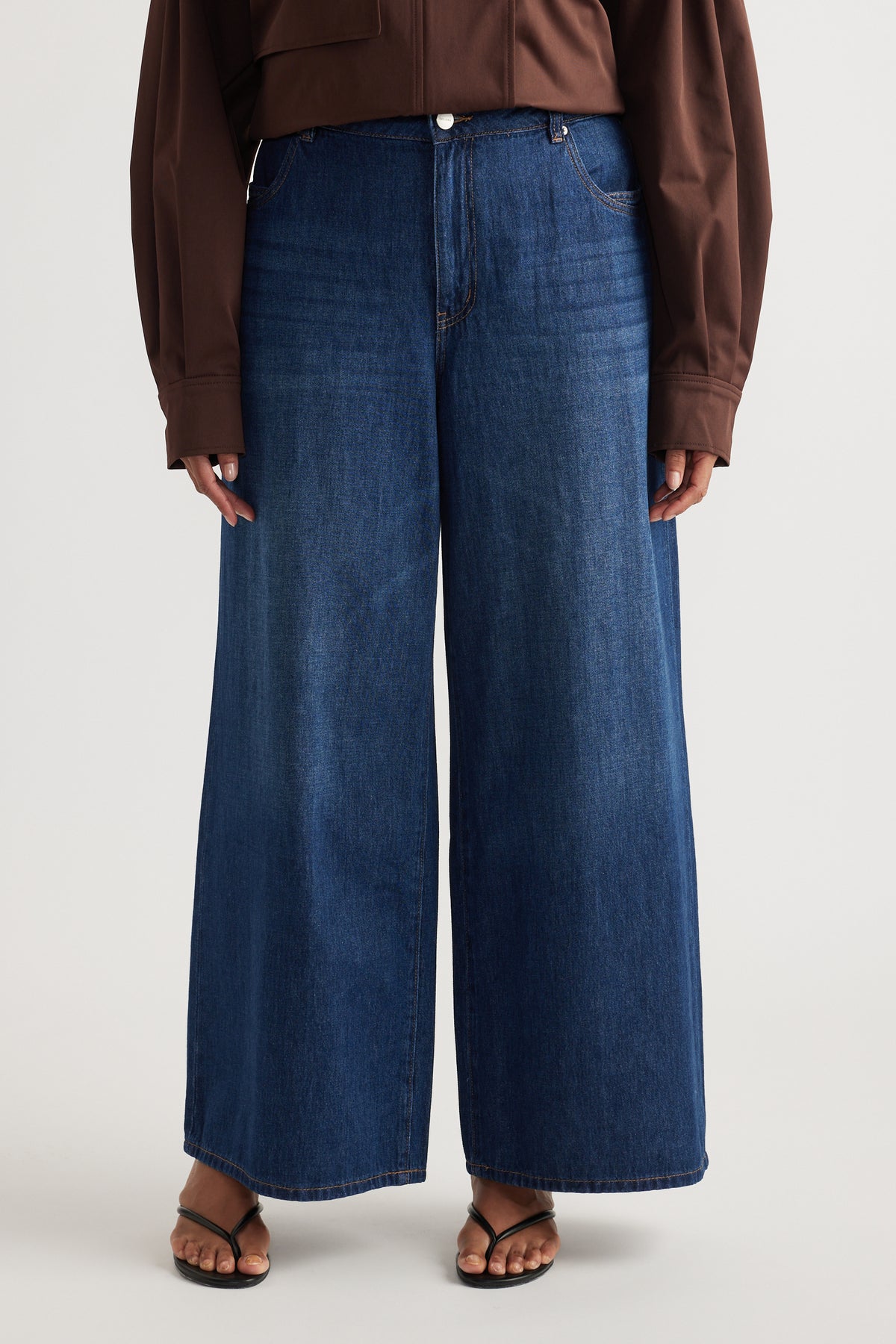 Woman wearing dark blue mid-rise wide-leg jeans with full-length hems, a brown top and flat sandals