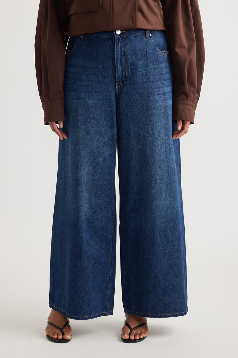 Woman wearing dark blue mid-rise wide-leg jeans with full-length hems, a brown top and flat sandals