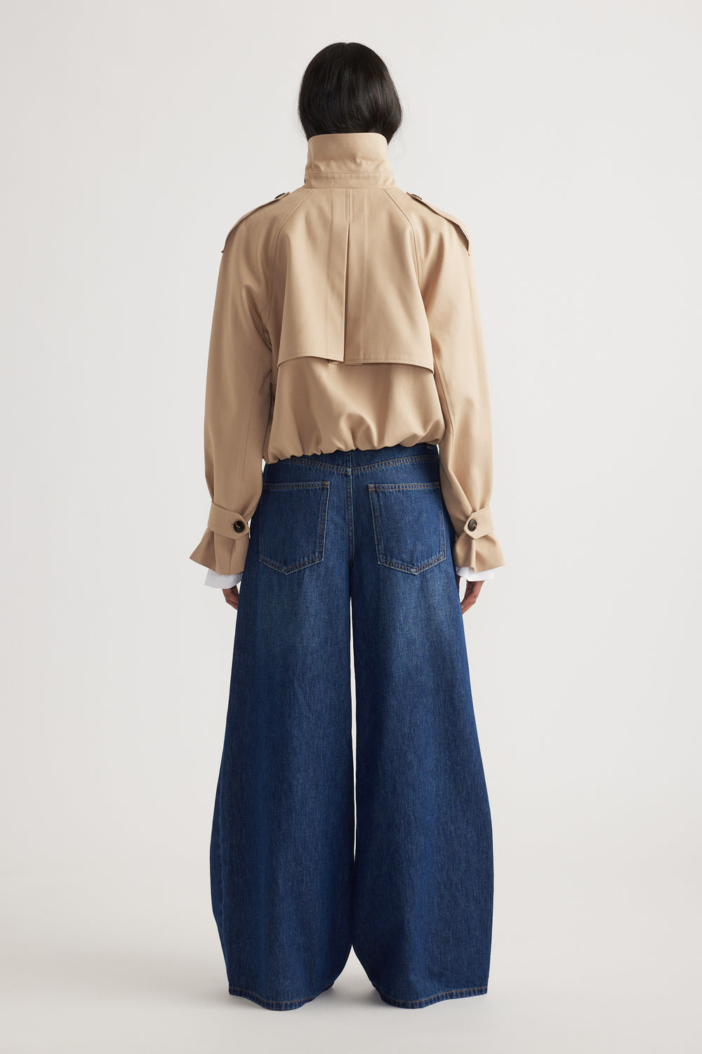 Woman wearing dark blue super wide leg jeans paired with a beige cropped jacket in a minimalist setting