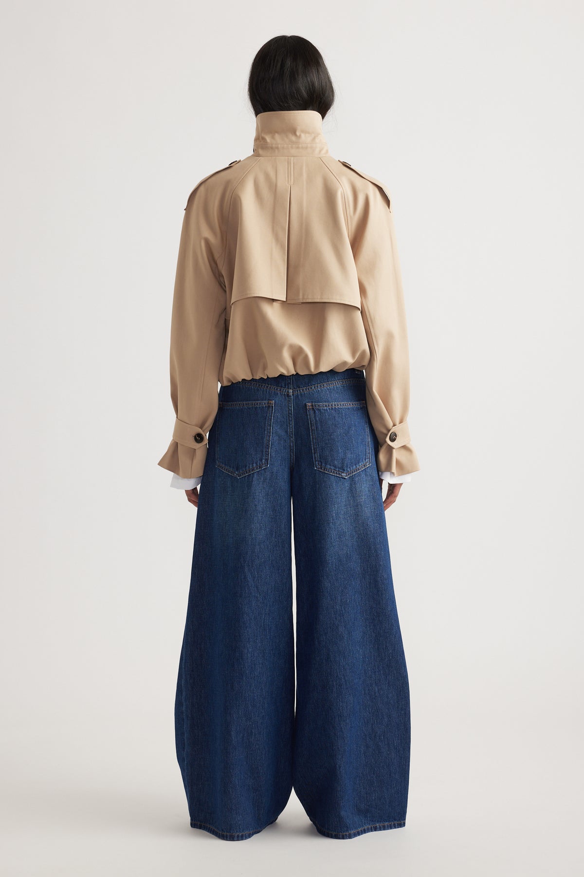 Woman wearing dark blue super wide leg jeans paired with a beige cropped jacket in a minimalist setting