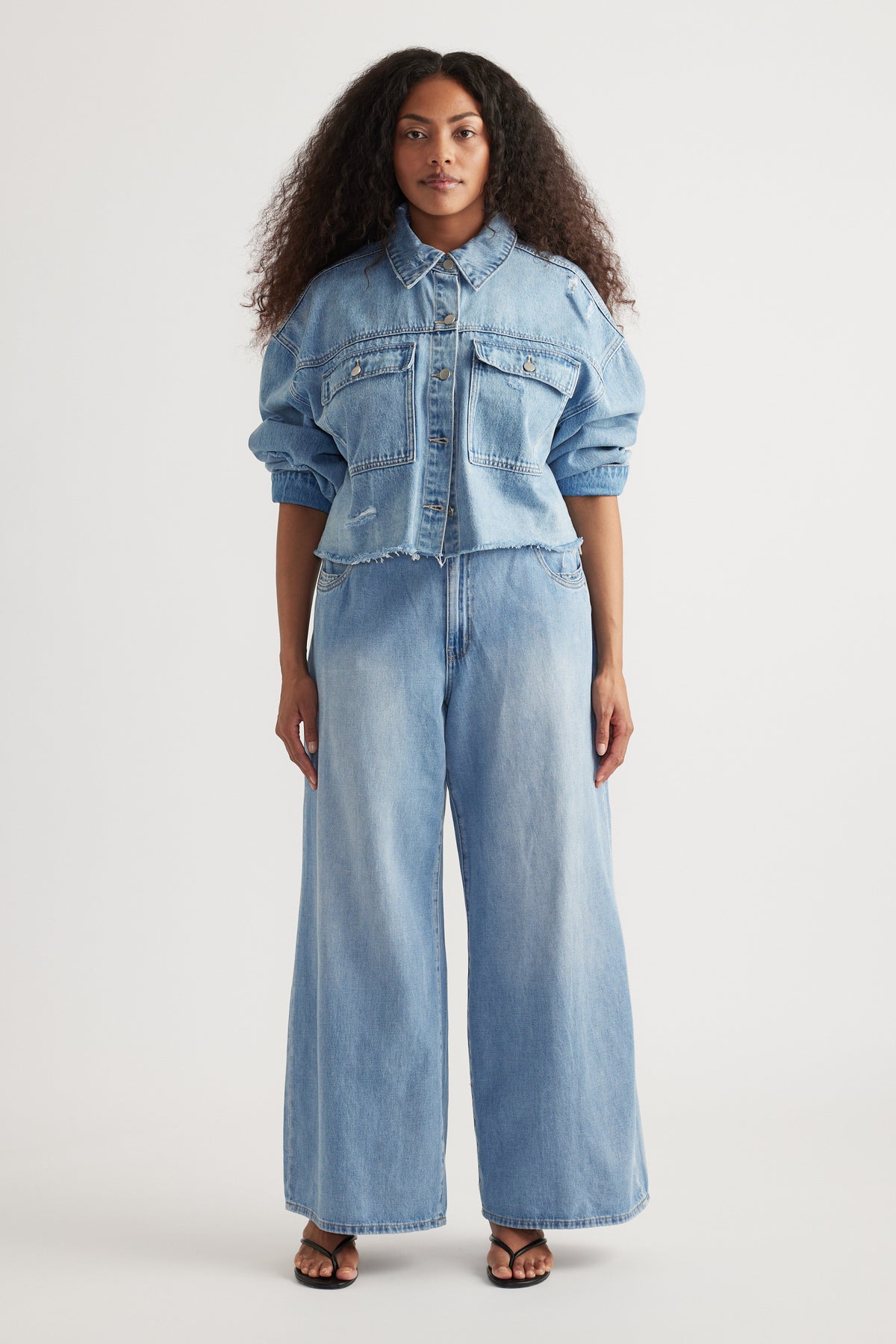 Woman wearing light wash wide leg jeans with a cropped denim shirt and flat sandals