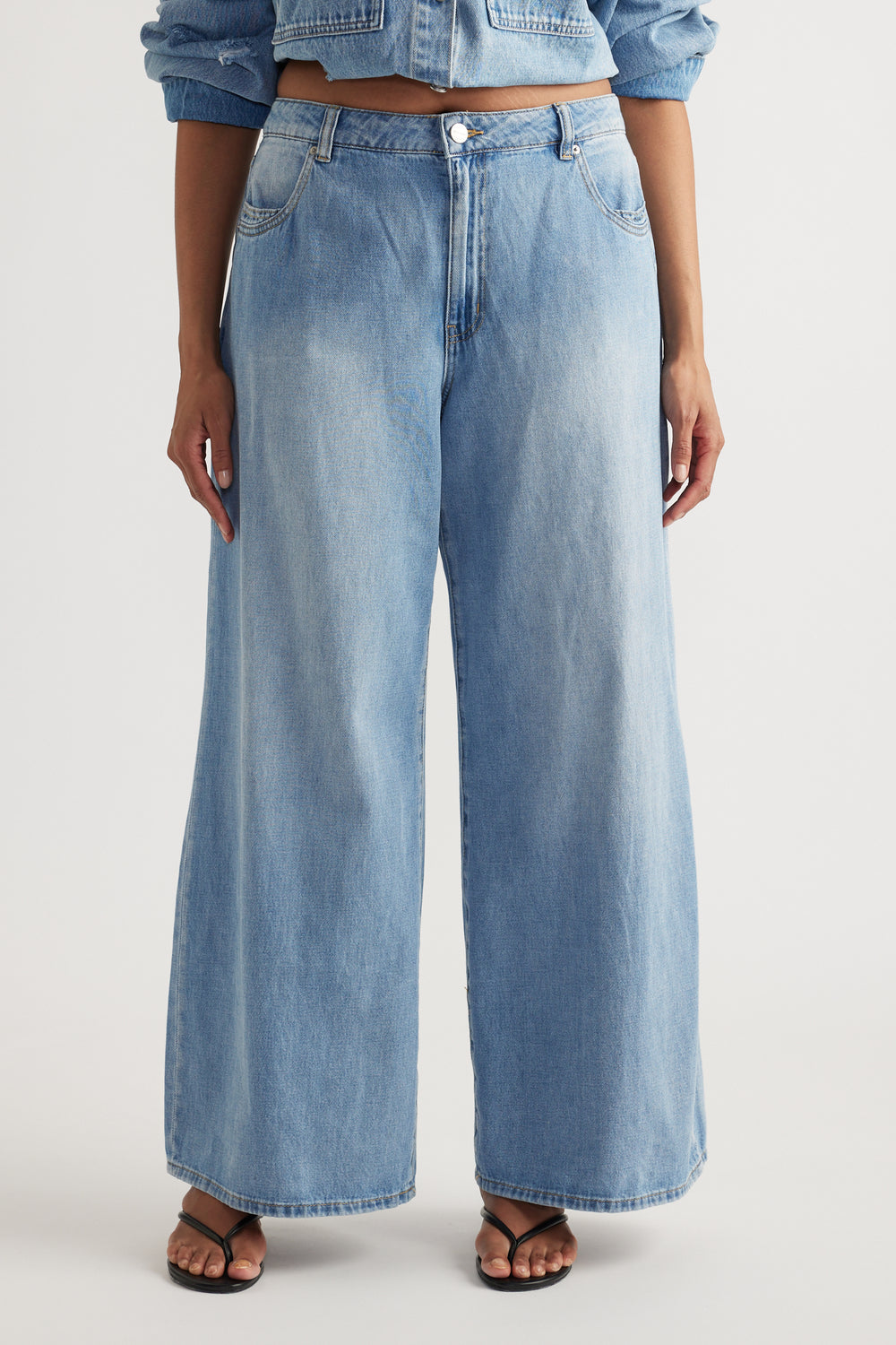 Woman wearing light blue mid rise super wide leg jeans with a cropped denim jacket and flat sandals