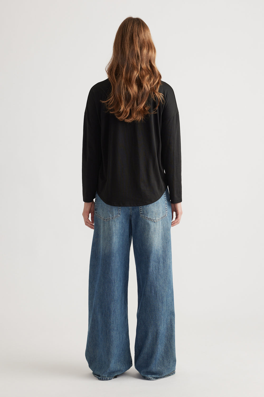 Woman wearing a relaxed black long sleeve top paired with wide-leg faded blue denim jeans for a casual look