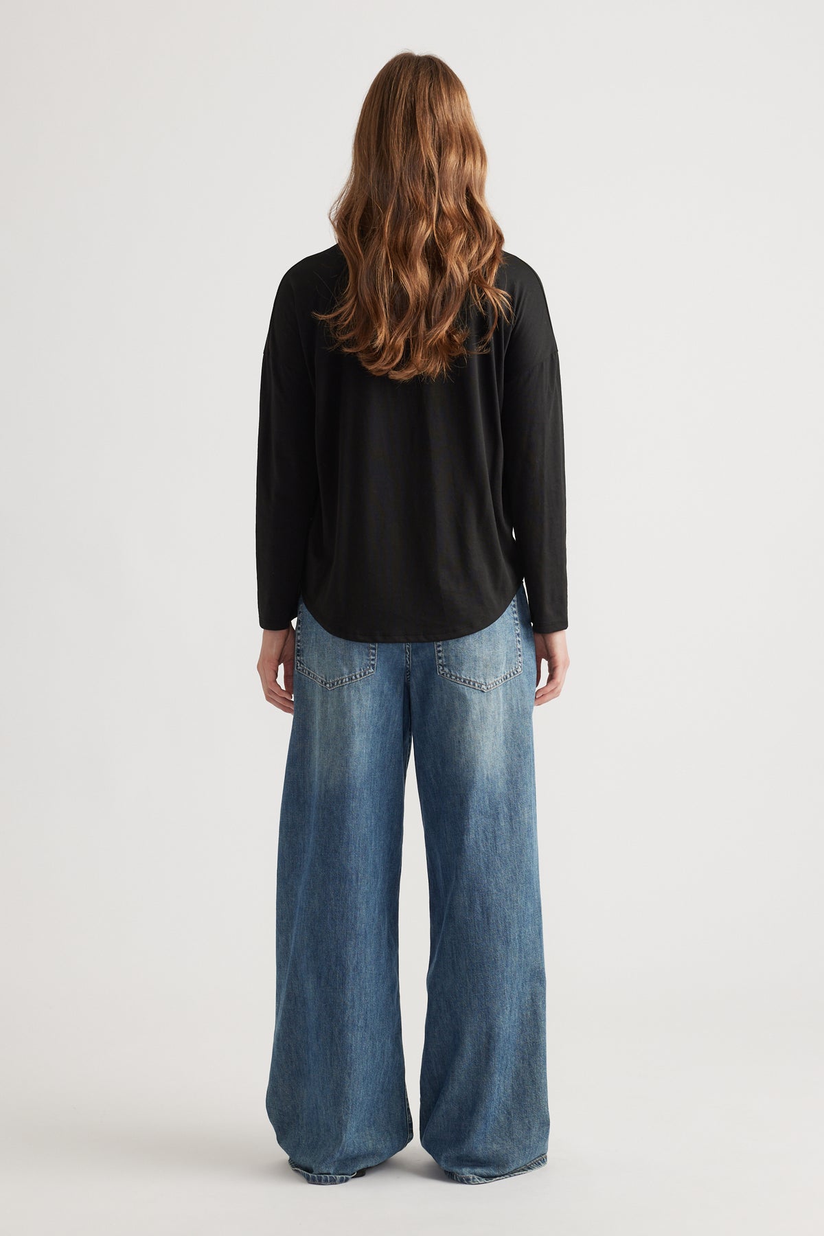Woman wearing a relaxed black long sleeve top paired with wide-leg faded blue denim jeans for a casual look