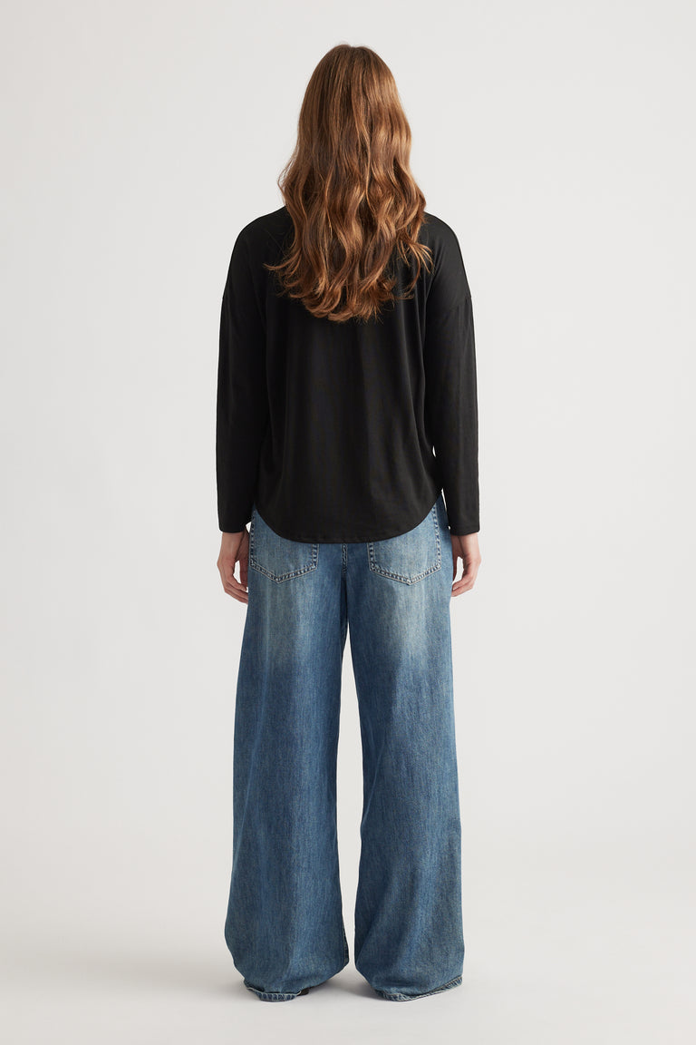 Woman wearing a relaxed black long sleeve top paired with wide-leg faded blue denim jeans for a casual look
