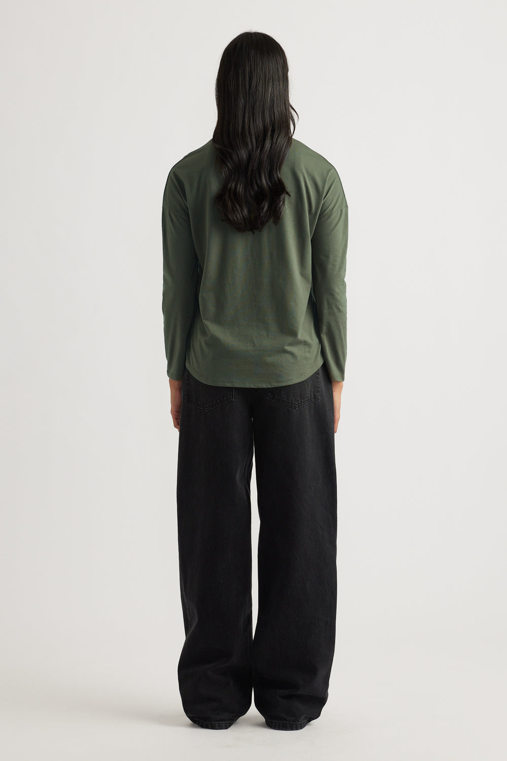 Woman with long dark hair wearing a fern green long sleeve top paired with relaxed wide-leg black pants