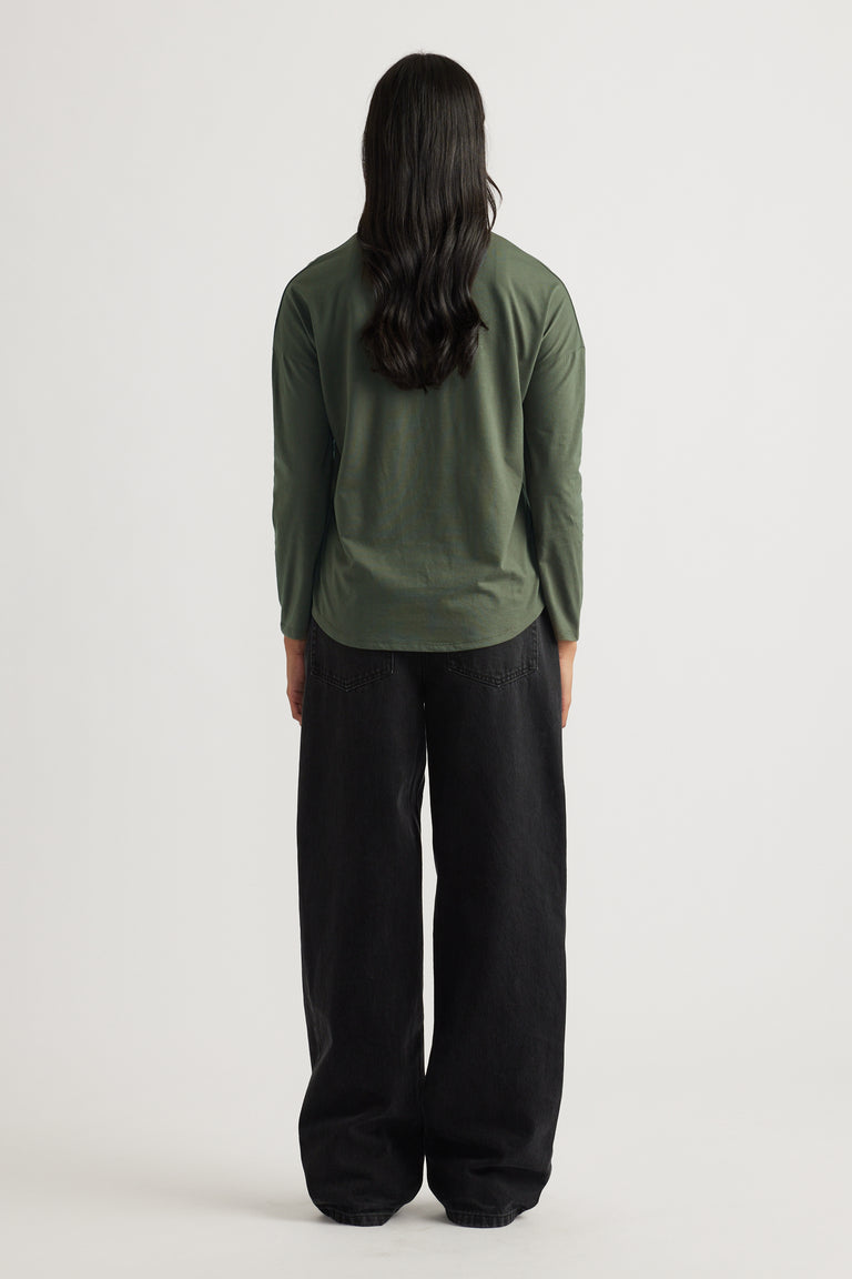 Woman with long dark hair wearing a fern green long sleeve top paired with relaxed wide-leg black pants