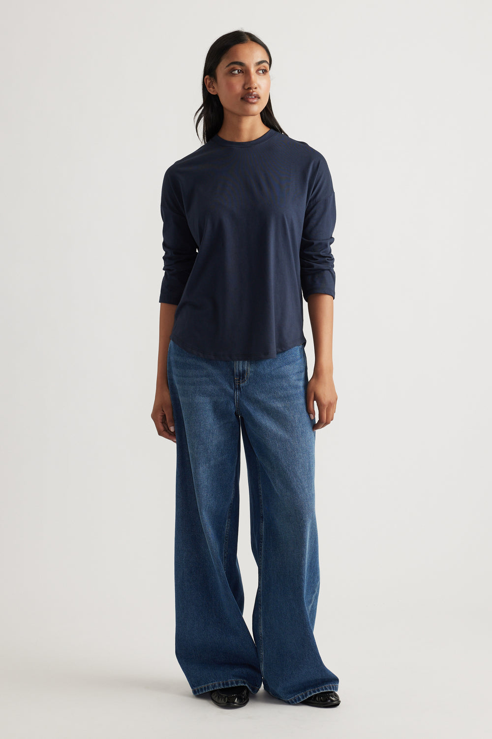 Woman wearing a navy long sleeve top paired with relaxed wide-leg classic blue denim jeans and black shoes