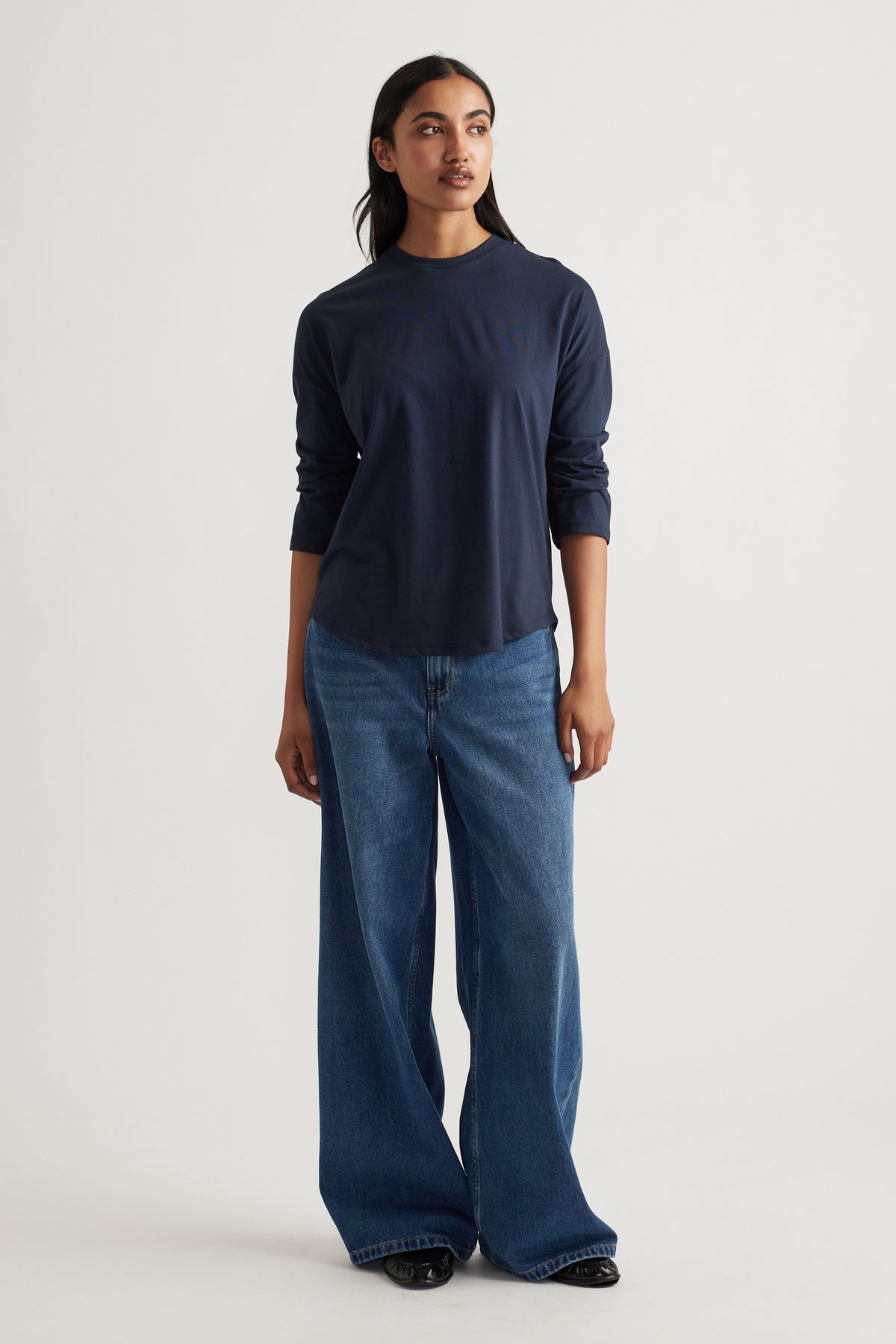 Woman wearing a navy long sleeve top paired with relaxed wide-leg classic blue denim jeans and black shoes