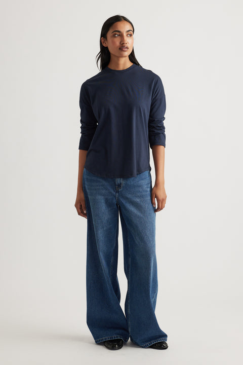 Woman wearing a navy long sleeve top paired with relaxed wide-leg classic blue denim jeans and black shoes