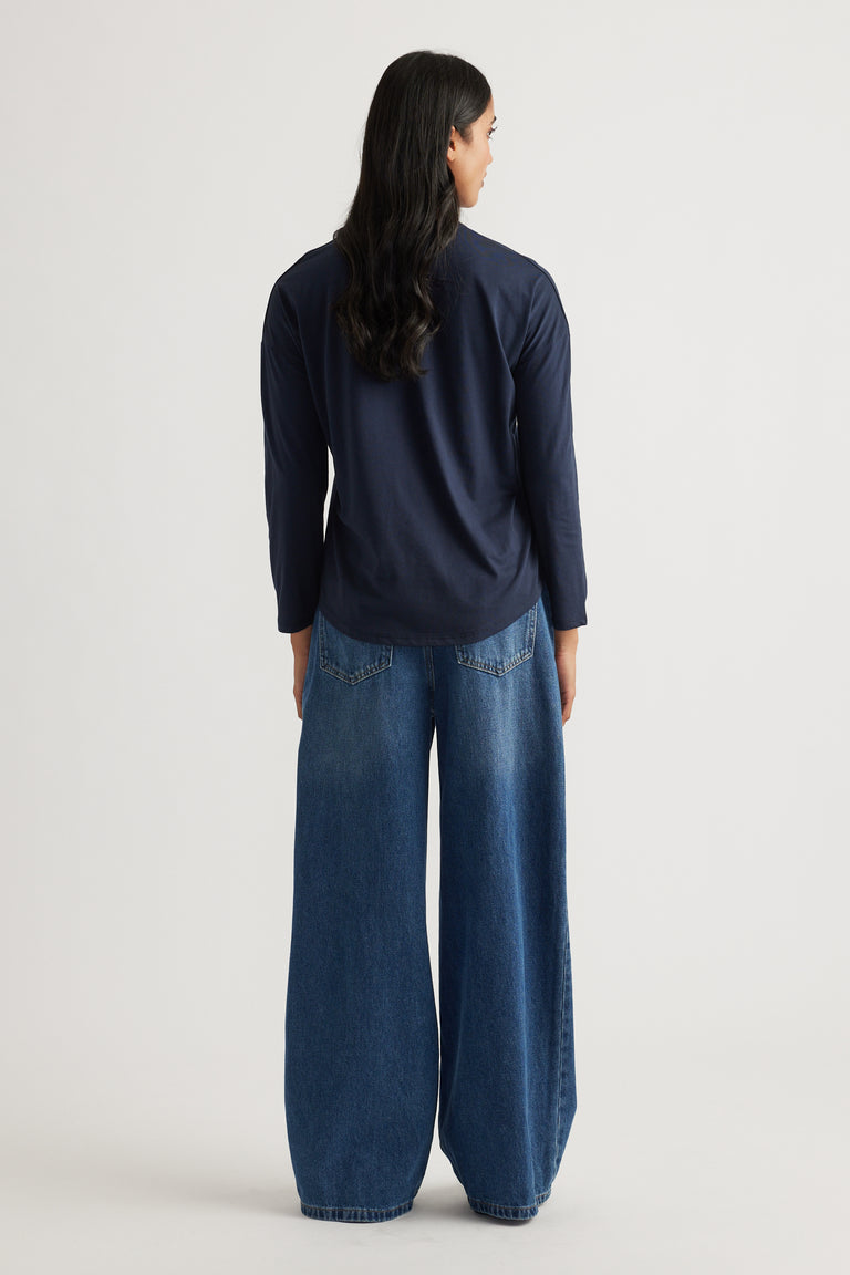 Woman shown from behind wearing a navy long sleeve top paired with loose wide-leg blue denim jeans against a neutral background