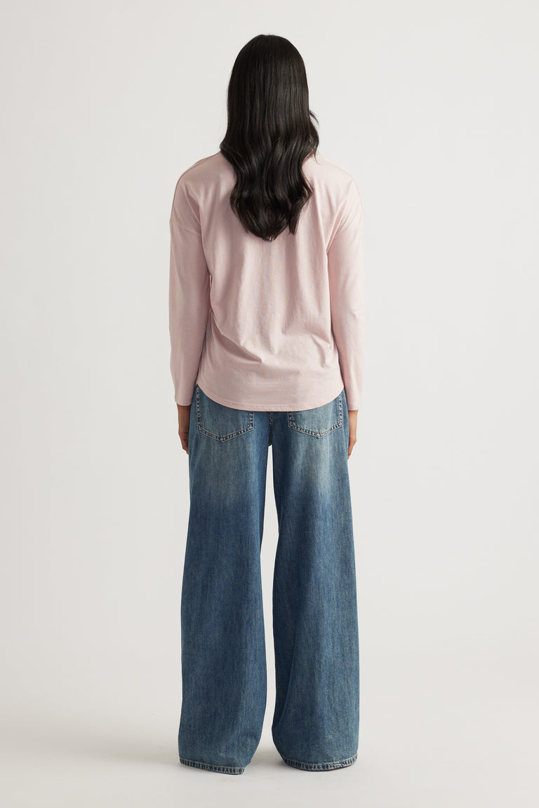 Person with long dark hair wearing a soft pink long sleeve top paired with wide-leg relaxed blue denim jeans viewed from behind