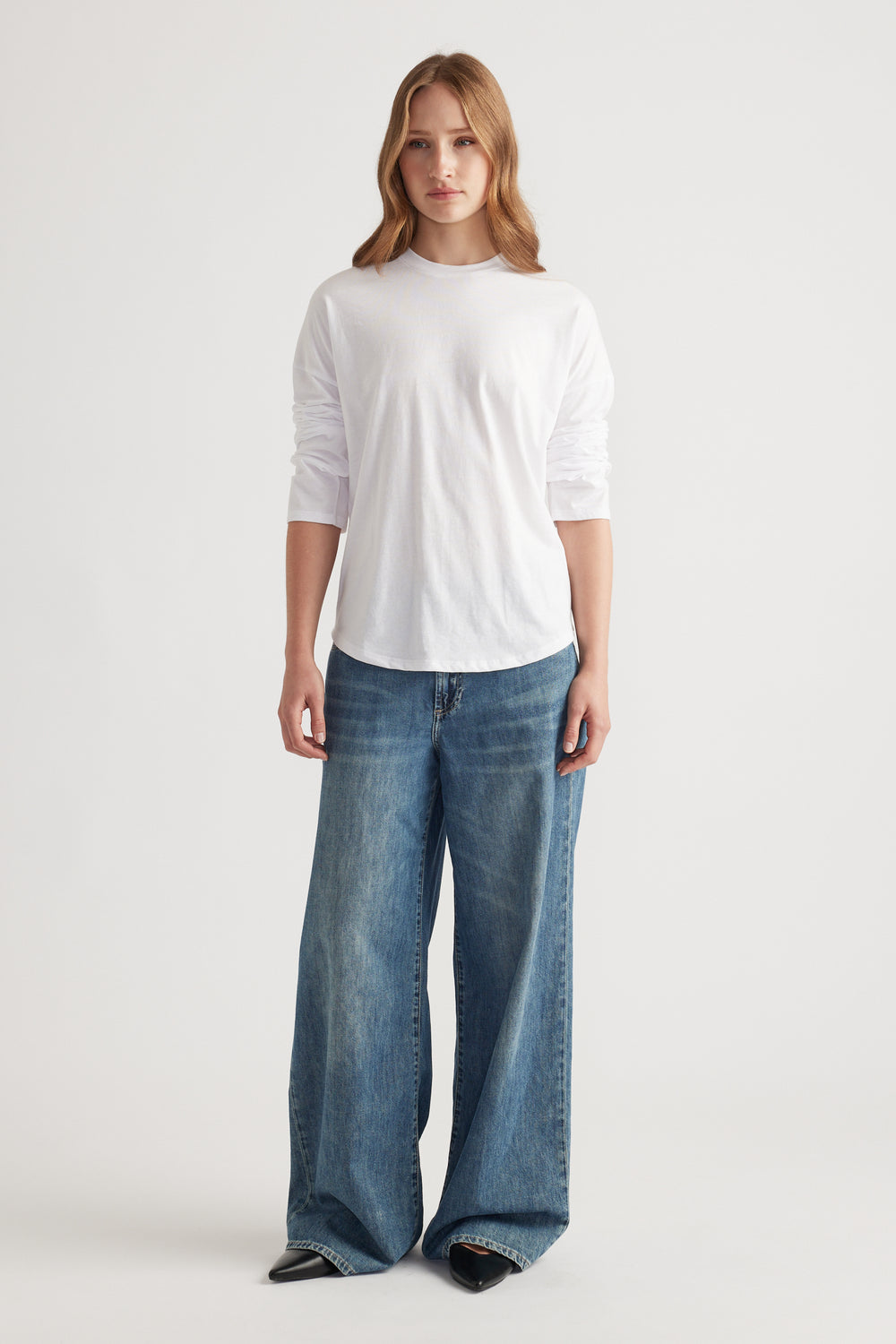 Woman wearing a classic white long sleeve top paired with loose wide-leg blue denim jeans and black pointed shoes