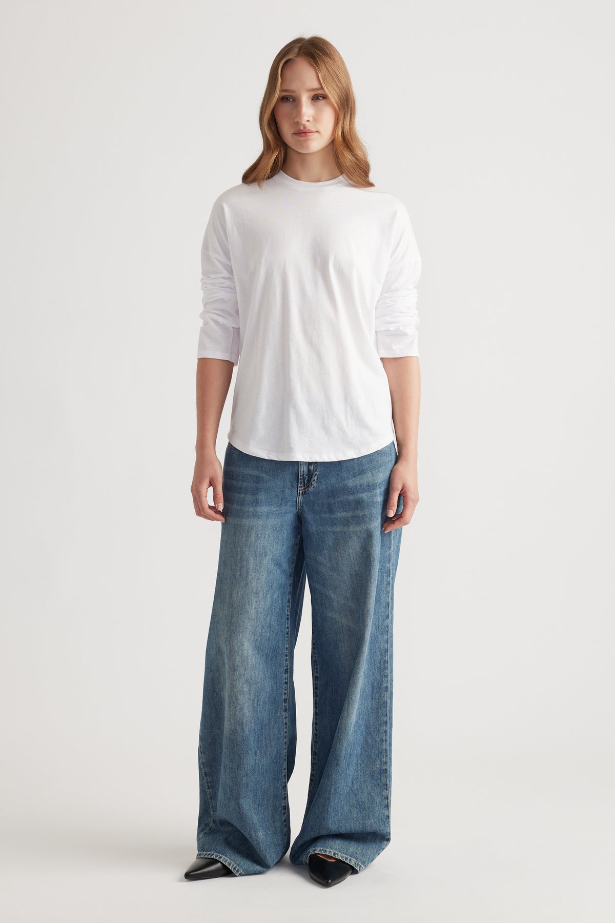 Woman wearing a classic white long sleeve top paired with loose wide-leg blue denim jeans and black pointed shoes