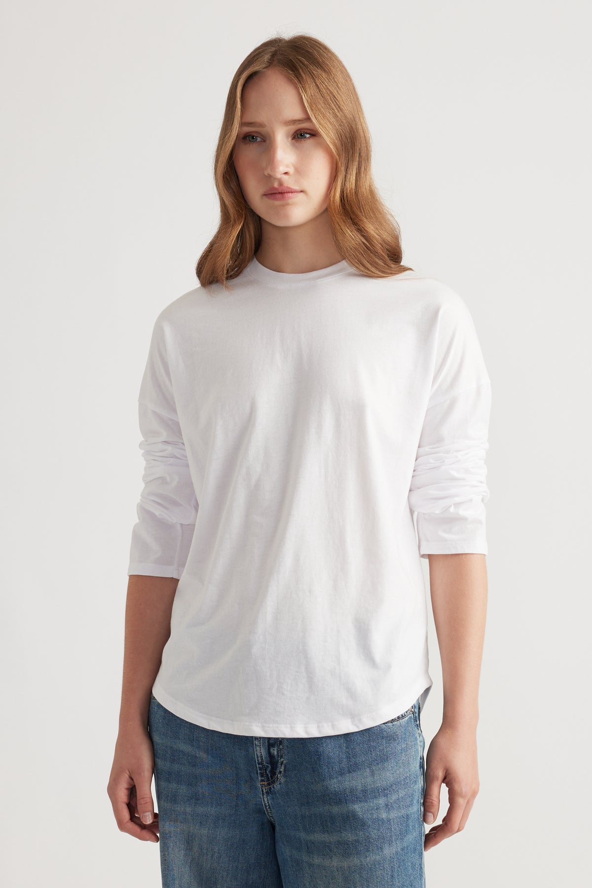 Young woman wearing a relaxed white long sleeve top paired with casual medium wash blue denim jeans