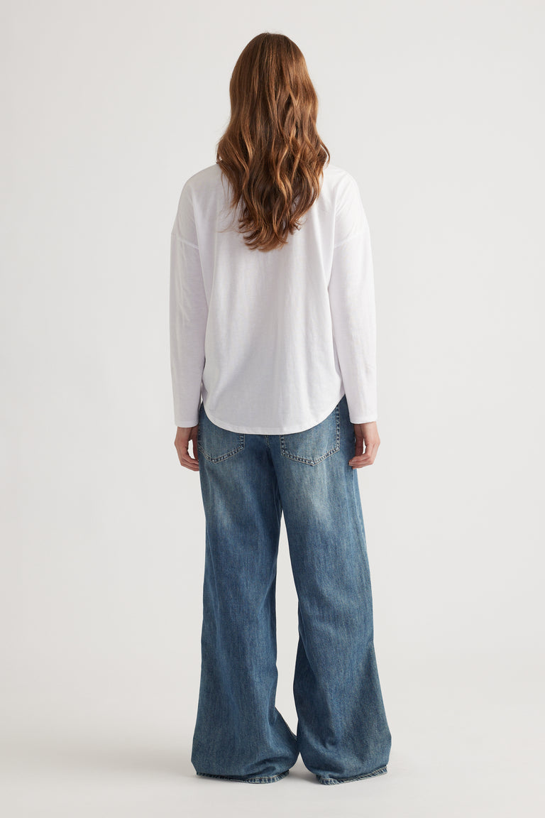 Woman with wavy hair wearing a relaxed white long sleeve top paired with wide-leg mid blue denim jeans from behind