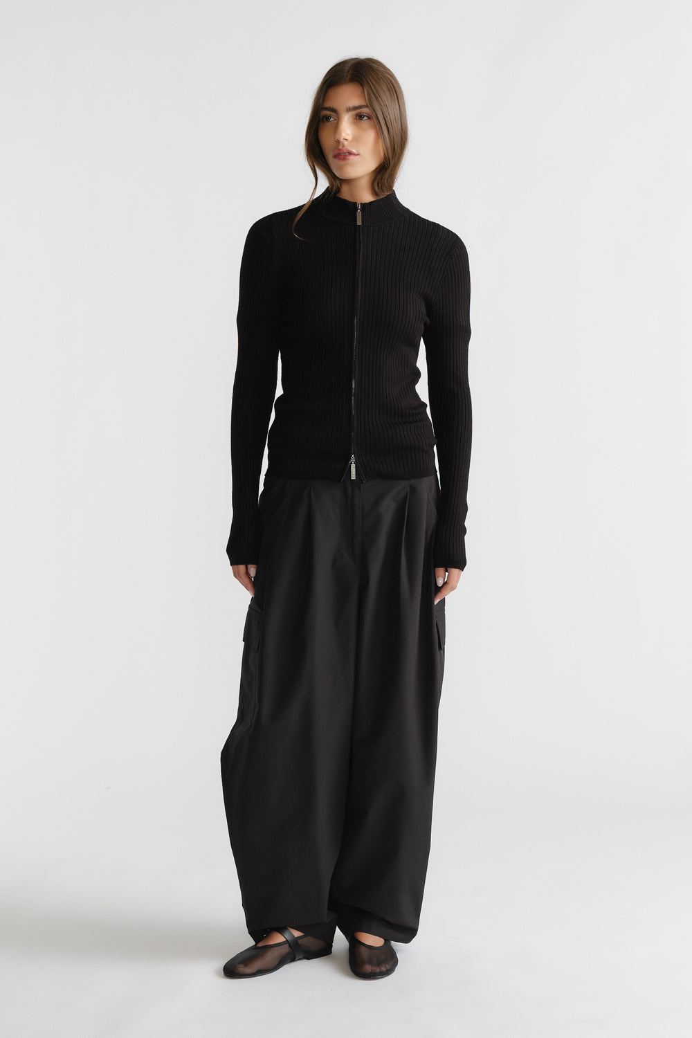 Woman in sleek black D-Luxe Knit Zip Long Sleeve with ribbed texture, paired with wide-leg pants for modern elegance.