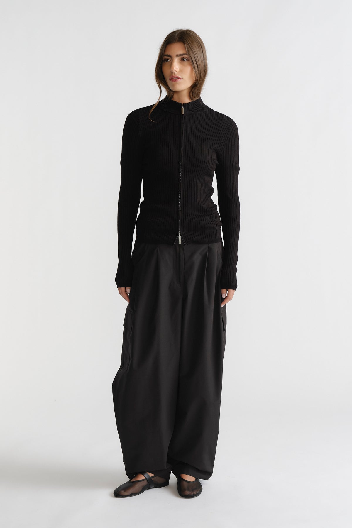 Woman in sleek black D-Luxe Knit Zip Long Sleeve with ribbed texture, paired with wide-leg pants for modern elegance.
